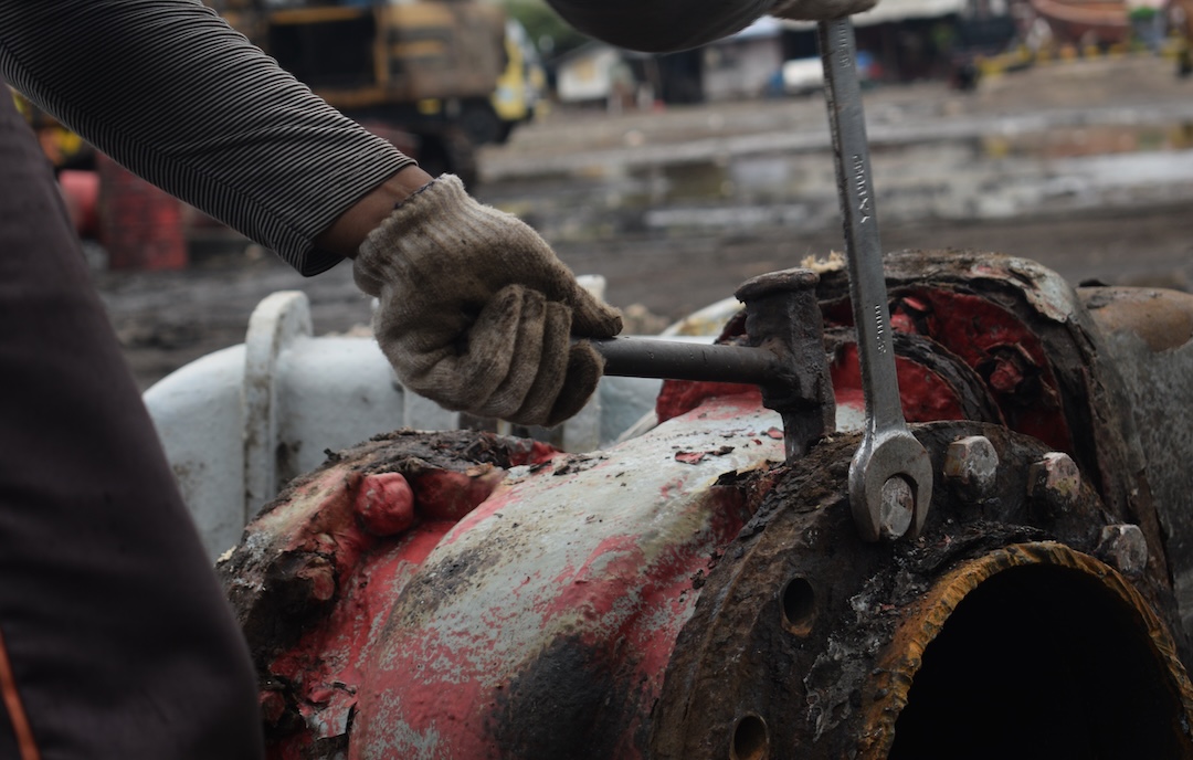 Close-up of hands using a spanner to loosen a bolt on industrial machinery